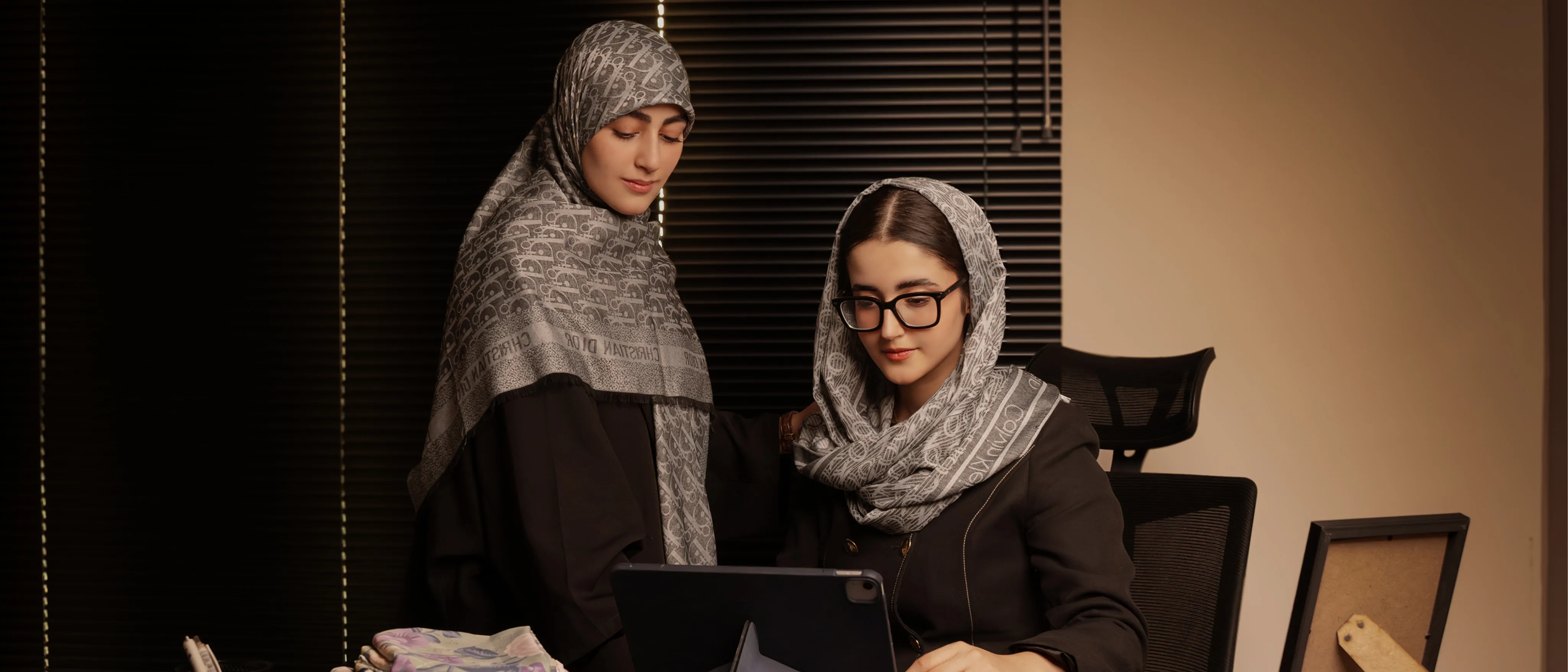 خانمی با روسری طرحدار و عینک، نشسته روی مبل چرمی به همراه تبلت