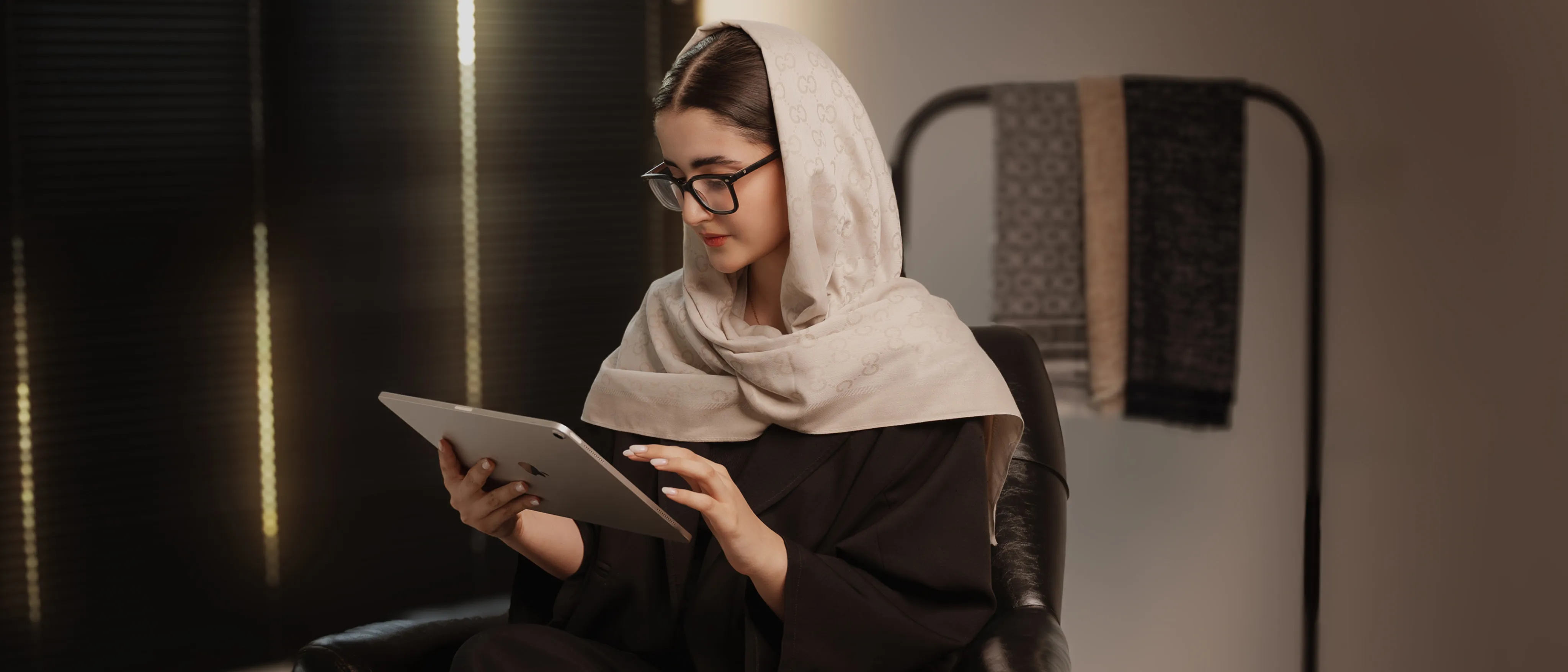 خانمی با روسری بژ طرحدار و عینک در حال استفاده از تبلت